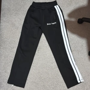 Svarta byxor från Palm Angels - Snygga svarta byxor från Palm Angels med vita ränder längs sidorna. Byxorna har en elastisk midja och en avslappnad passform, perfekt för en stilren look.