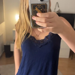 Mörkblå linnetopp med spetsdetaljer - Säljer en mörkblå linnetopp med vackra spetsdetaljer vid halsringningen. Toppen har smala axelband och en bekväm passform, perfekt för varma dagar.