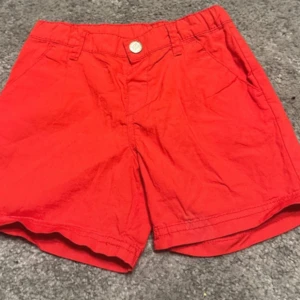 Röda shorts med knapp - Snygga röda shorts med knapp och fickor fram och bak. Perfekta för sommardagar och avslappnade tillfällen. De har en klassisk design med en bekväm passform.