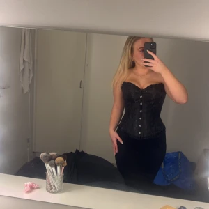 Svart korsett med snörning - Snygg svart korsett med snörning framtill. Perfekt för en kväll ute eller en speciell tillställning. Den har en elegant design som framhäver figuren.