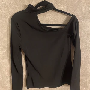 Svart långärmad topp från SHEIN - Snygg svart långärmad topp från SHEIN med unik asymmetrisk design och ribbad textur. Perfekt för en trendig look med sin öppna axeldetalj. Passar bra till både jeans och kjol.🥀