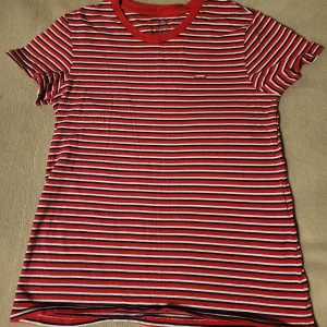 Randig t-shirt från Levi's - Snygg randig t-shirt från Levi's i rött, vitt och blått. Den har en klassisk rund halsringning och korta ärmar. Perfekt för en avslappnad stil.