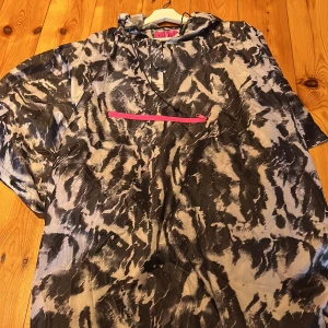 Mönstrad vindjacka från Mywear Active - Säljer en cool vindjacka från Mywear Active med ett unikt svart och grått mönster. Jackan har en praktisk dragkedja i rosa framtill och en justerbar huva. Perfekt för aktiva dagar utomhus.