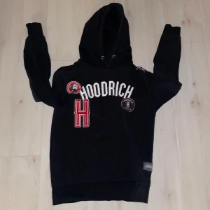 Svart hoodie från Hoodrich - Snygg svart hoodie från Hoodrich med tryck i vitt och rött. Den har en stor ficka framtill och en justerbar huva. Perfekt för en avslappnad stil.