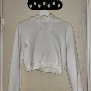 Vit croppad hoodie från NY Trend - Säljer en stilren vit croppad hoodie från Nelly Trend. Den har en klassisk huva och långa ärmar. Perfekt för en avslappnad look.