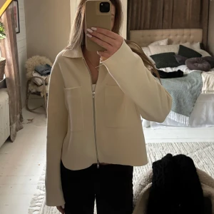 Beige jacka från Åhléns - Snygg beige jacka från Åhléns med dragkedja framtill och två stora fickor. Jackan har en klassisk krage och långa ärmar, använd en gång och därav mycket bra skick!