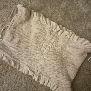 Vit tubtopp från Bik Bok - Säljer en söt vit tubtopp från Bik Bok i storlek XS. Toppen har en smockad design med volangdetaljer upptill och nedtill, vilket ger en romantisk touch. Perfekt för sommardagar eller som en del av en lager-på-lager-look.