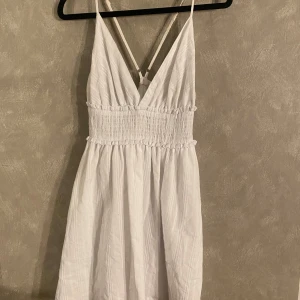 Vit sommarklänning med smockdetaljer - Säljer en söt vit klänning från shein med smockdetaljer i midjan och smala axelband. Klänningen har en v-ringad design och är perfekt för varma sommardagar. Den är tillverkad i ett lätt och luftigt material. 😊
