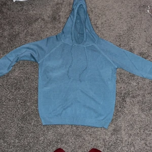 Blå merinoull hoodie - Säljer en stilren blå hoodie med dragsko i huvan. Perfekt för en avslappnad look. Den har långa ärmar och ribbade muddar vid ärmslut och nederkant. Merinoull, helt ny. Pris kan diskuteras vid snabbt köp. Slim fit