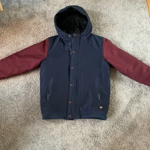 Blå och vinröd jacka från Vans - Säljer en snygg blå och vinröd jacka från Vans i storlek 164. Jackan har en huva och stängs med dragkedja och knappar. Perfekt för kyligare dagar med sin långa ärmar och stilrena design. Inge defekter förutom en liten fläck på vänster arm, inget man ser om man inte kollar nära.
