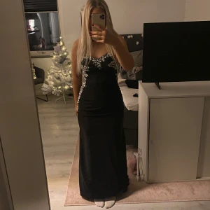 Svart långklänning med paljettdetaljer - Säljer min gamla balklänning🩷 Elegant svart långklänning med glittrande paljettdetaljer längs byst och sidor. Klänningen har en öppen rygg och är axelbandslös. Mina mått är- Längd- 170cm. Byst-94 cm. Midja-74. Höft-100. Klänningen går att justeras i bredden över ryggen. Den är även uppsydd längst ner men det går att ta ut igen. Skriv för mer frågor 🩷