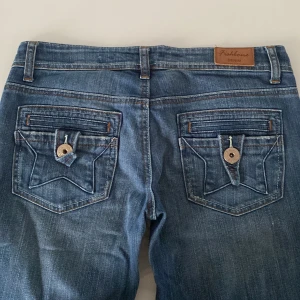 Blå jeans från Fashion Denim - Snygga blå jeans från Fashion Denim med klassisk femficksdesign och dekorativa sömmar på bakfickorna. Jeansen har en knappgylf och bälteshällor, perfekt för en avslappnad stil.
