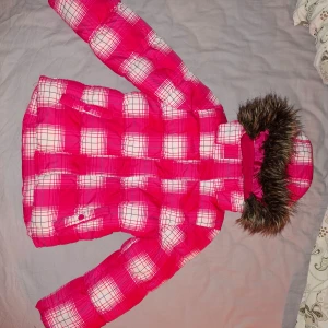 Rutig rosa vinterjacka avtagbar huva och päls Cubus  - Säljer en cool rosa vinterjacka med rutigt mönster och en mysig pälsdetalj på huvan. Jackan har långa ärmar med ribbade muddar och en praktisk dragkedja framtill. Perfekt för att hålla sig varm och stilren under kyliga dagar. #barnkläder #vinterjacka #rosa 