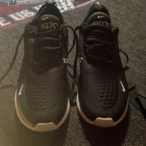 Svarta Nike Air 270 sneakers - Säljer ett par svarta Nike Air 270 sneakers med vit sula. Skorna har snörning och en luftig design för extra komfort. Perfekta för både träning och vardag.