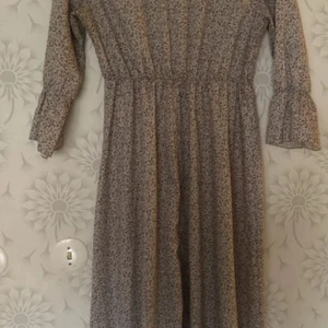 Blommig långklänning - Charmig långklänning med blommigt mönster i dämpade färger. Klänningen har trekvartsärmar och en smickrande passform med resår i midjan. Perfekt för en avslappnad och stilfull look.