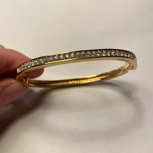 Swarovski armband guldfärgad med glittriga stenar - Elegant vintage armband  från USA med en rad av glittriga stenar längs ovansidan. Armbandet har en smidig låsmekanism och en stilren design som passar perfekt för speciella tillfällen.