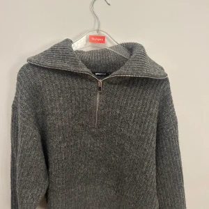 Grå stickad tröja från Ginatricot - Mysig grå stickad tröja från Ginatricot med dragkedja vid halsen. Perfekt för kyliga dagar med sin ribbade design och långa ärmar. En stilren och bekväm tröja för alla tillfällen.