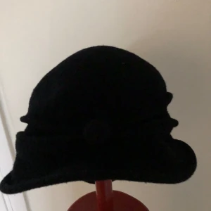 Svart ullhatt med dekorativ kant - Elegant svart hatt i ren ny ull från Woolmark. Hatten har en dekorativ kant och en klassisk design som passar perfekt för kyligare dagar. Den är både stilren och praktisk.