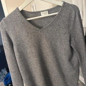 Grå tröja från VILA - Snygg och enkel grå tröja från VILA med v-ringning. Perfekt för en stilren look. Tröjan har långa ärmar och ribbade kanter vid ärmslut och nederkant.