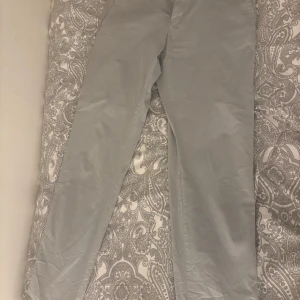 Grå kostymbyxor från Tommy Hilfiger - Snygga grå kostymbyxor från Tommy Hilfiger med en elegant och stilren design. Byxorna har knappar bak och är perfekta för en dressad look. Passar utmärkt för både formella och semi-formella tillfällen.