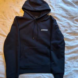 Säljer en stilren svart hoodie från Jacquemus med logga på bröstet. Den har en klassisk känguruficka och justerbar huva med snören. Perfekt för en avslappnad look. Inget kvitto men skickar gärna fler bilder för att bevisa äktighet, en liten missfärgning på fickan, se bild 5!