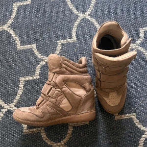 Beige sneakers med kilklack isabel marant liknande - Snygga beige sneakers med kilklack som liknar isabel marant! Skorna har rätt slitna sulor på insidan men det är lätt att ersätta! Köpta second hand och väldigt skjöna att gå i☺️Storlek 37 men passar mer spm 38!!