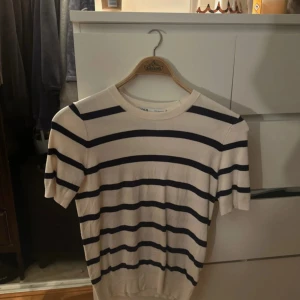 Randig kortärmad tröja från Zara - Säljer en stilren randig tröja från Zara i beige och svart. Tröjan är kortärmad och har en klassisk rund halsringning. Perfekt för en avslappnad look.