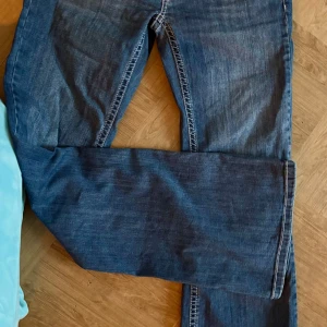 Blå jeans från Nelly - Snygga blå jeans från Nelly med bootcut-stil och dekorativa sömmar på bakfickorna. De har en hög midja och stängs med två knappar framtill. Perfekta för en avslappnad look.