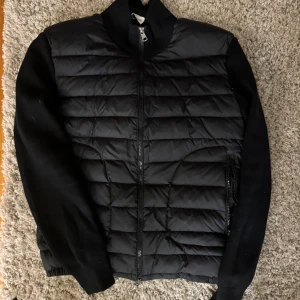 Svart quiltad jacka från Moncler - Snygg svart quiltad jacka från Moncler med dragkedja och långa ärmar. Perfekt för kyligare dagar med sin stilrena design och varma material.
