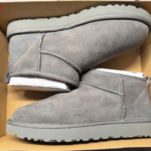 Grå mocka boots från UGG - Säljer ett par ultra mini i grey från UGG i mjuk mocka. De är helt nya och oanvända, köpte fel storlek och hann ej lämna tillbaka dem. Perfekta för kyligare dagar med sin bekväma och varma design. De har en klassisk stil med rund tå och en robust sula. Om du har några frågor eller funderingar är det bara att höra av dig 