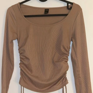 Beige ribbad topp från SHEIN - Snygg beige ribbad topp från SHEIN med långa ärmar och rynkade detaljer på sidorna. Perfekt för en stilren look.