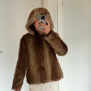 Brun pälsjacka med huva - Säljer en mysig brun pälsjacka med huva. Jackan har en fluffig och varm design, perfekt för kyliga dagar. Passar perfekt på mig som är mellan xs-s med en oversized look. Tyvärr saknar den EN knapp, se sista bild. 