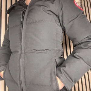 Svart dunjacka från Canada Goose - Säljer en svart dunjacka från Canada Goose (model:Chelsea parka)med pälskantad huva. Jackan har en dragkedja framtill och är långärmad. Perfekt för kalla vinterdagar. (Storlek XXS)