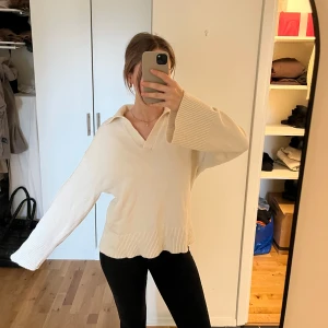 Benvit stickad tröja med krage - Säljer en stilren beige stickad tröja med krage och v-ringning. Tröjan har långa ärmar och ribbade detaljer vid ärmslut och nederkant. Super skön, lite skrynklig på bilderna, använd fåtal gånger 