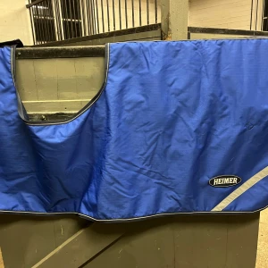 Vattenavvisande skritt täcke till häst - Blått vattenavvisande skritt täcke. Är även fleecefodrat och har ett reflexsträck på varje sida. Mycket bra skick, inga hål eller defekter. Nytvättat men finns lite vita hårstrån. Kan behövas impregneras (eftersom det är nytvättat). Storlek full. 