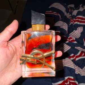 Parfym från Yves Saint Laurent - en elegant parfymflaska med en distinkt rektangulär form och en gyllene YSL-logotyp som pryder framsidan. parfymen är fylld med en djup bärnstensfärgad vätska, doft på parfymen är exotiskt vanilj. perfekt för den som söker en lyxig, stilren doftupplevelse & vibe! använt fåtal gånger, kan mötas upp annars står köparen för frakten🩷
