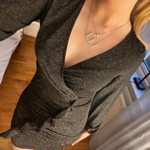 Svart glittrig nyårsklänning - Snygg svart omlottklänning med glittrigt mönster. Perfekt klänning till nyår, endast använd 1 gång💗💗