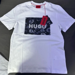 Vit t-shirt från Hugo - Snygg vit t-shirt från Hugo med ett svart tryck av rosor och texten 'HUGO' på bröstet. Perfekt för en stilren look.
