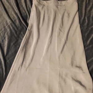 Grå lång kjol från OVS - Säljer en stilren grå kjol från OVS. Klänningen har en elegant och enkel design, perfekt för olika tillfällen. Den är i en mjuk och bekväm polyesterblandning.