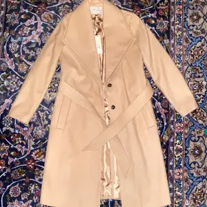 En snygg beige kappa från River Island som är i nyskick med prislapp (originalpris 1075kr).  Varken fickorna eller slitsen där bak är sprättade. Om du har några ytterligare frågor så skriv gärna 😊