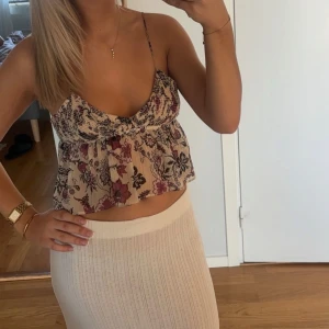 Blommig croppad linnetopp - Söt blommig croppad linnetopp med smala axelband och volangdetaljer. Perfekt för varma sommardagar.