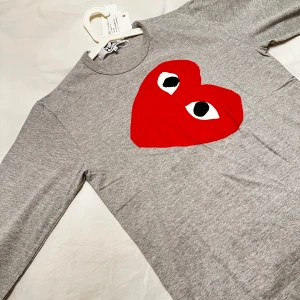 Grå tröja från Comme des Garçons Play - Snygg grå tröja från Comme des Garçons Play med det ikoniska röda hjärtat med ögon på bröstet. Perfekt för en stilren och modern look. Helt ny med prislappen kvar. 
