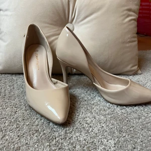Beige klackar från Jenny Fairy - Eleganta och glansiga beige klackar från Jenny Fairy med spetsig tå och hög klack. Perfekta för en stilren look. Storlek 38 men känns mer som 39.
