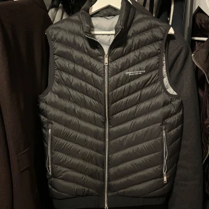 Armani Exchange Väst - Tja, säljer västen för den kommer inte till så mycket användning. Köpte den i våras, används ett tiotal gånger. Pris går att diskuteras vid snabb affär.  185 cm  Storlek M  Armani Exchange GILET  PIUMINO Nypris: 1500