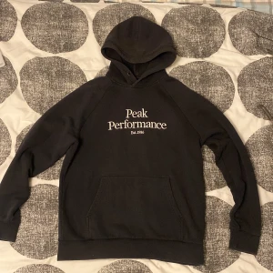 Svart hoodie från Peak Performance - Säljer en svart hoodie från Peak Performance med vit text på framsidan. Perfekt för en avslappnad stil. Använd cirka 10 gånger, inga skador eller defekter, är i bra skicka och redo att användas. Storlek XL men passar även L 