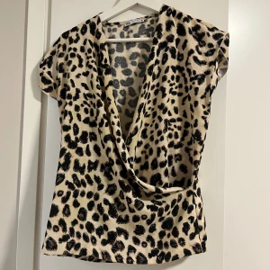 Leopardmönstrad omlottopp - Snygg leopardmönstrad omlottopp från Zara med djup v-ringning. Toppen har korta ärmar och ett trendigt omlottdesign som ger en stilfull look. Perfekt för att sticka ut i mängden!
