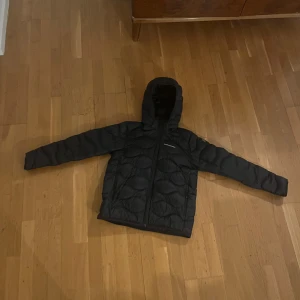 Svart quiltad jacka med huva - Säljer en svart quiltad jacka från Peak Performance. Jackan har en huva och dragkedja framtill. Perfekt för kyligare dagar.
