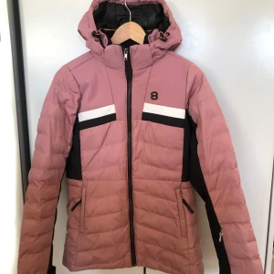 Rosa jacka från 8848 Altitude - Snygg rosa jacka från 8848 Altitude med svarta och vita detaljer. Jackan har en dragkedja framtill och praktiska fickor. Perfekt för kyliga dagar med sin långa ärmar och justerbara huva.