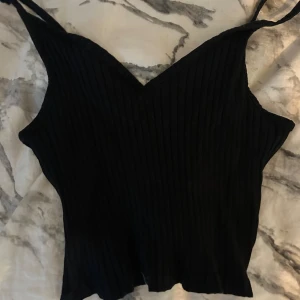 Svart ribbad linnetopp - Snygg svart ribbad linnetopp med smala axelband. Perfekt för en stilren look. Passar bra till både jeans och kjol.