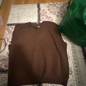Brun väst från H&M Divided - Säljer en brun väst från H&M Divided. Västen har en enkel design med rund hals och är ärmlös, perfekt för lager-på-lager under höst och vår.